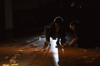 foto: dos personas cerca del suelo, al lado una fila de símbolos conformados con piezas de madera